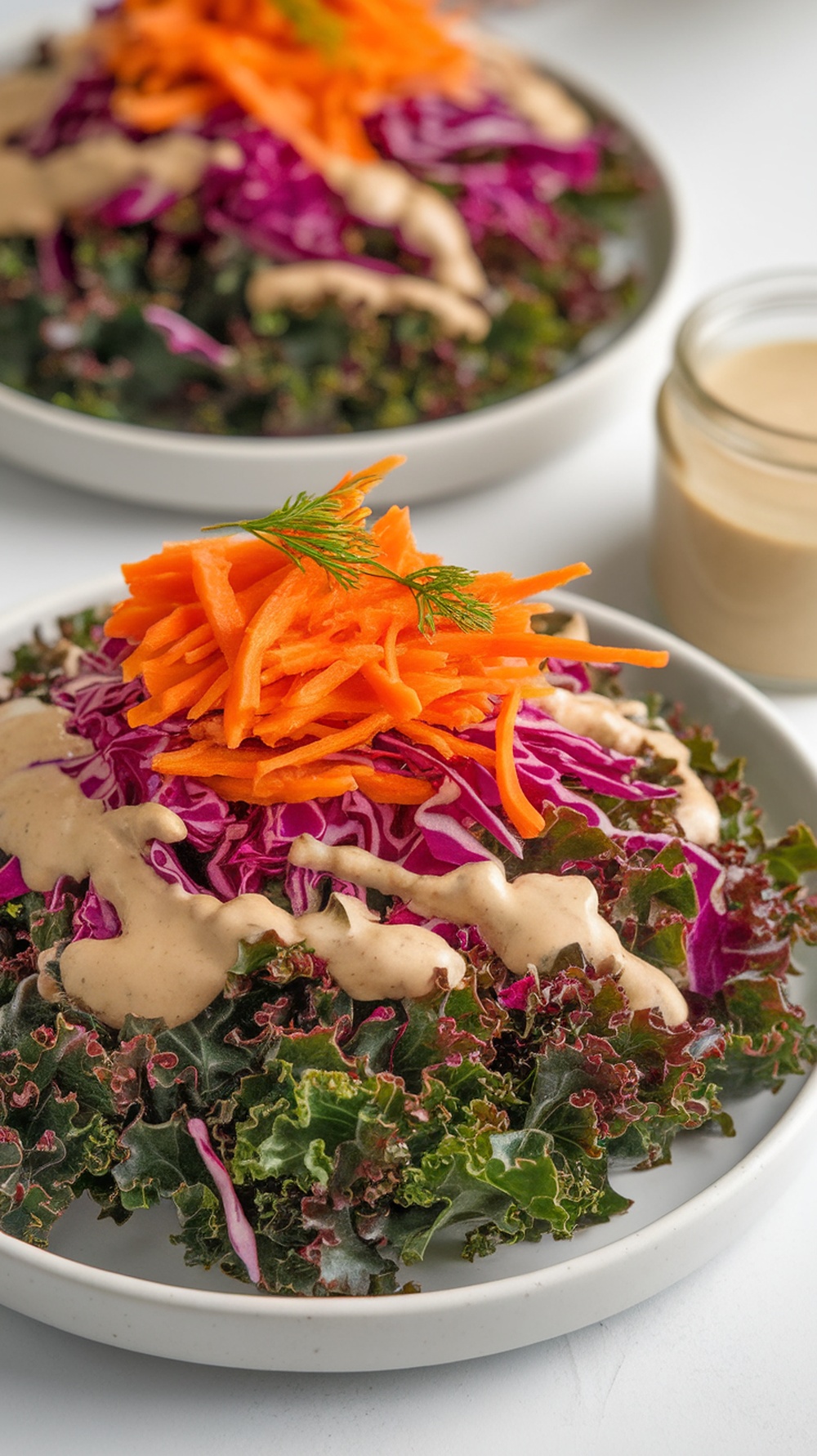 A vibrant rainbow kale salad topped with grated carrots and a creamy tahini dressing.