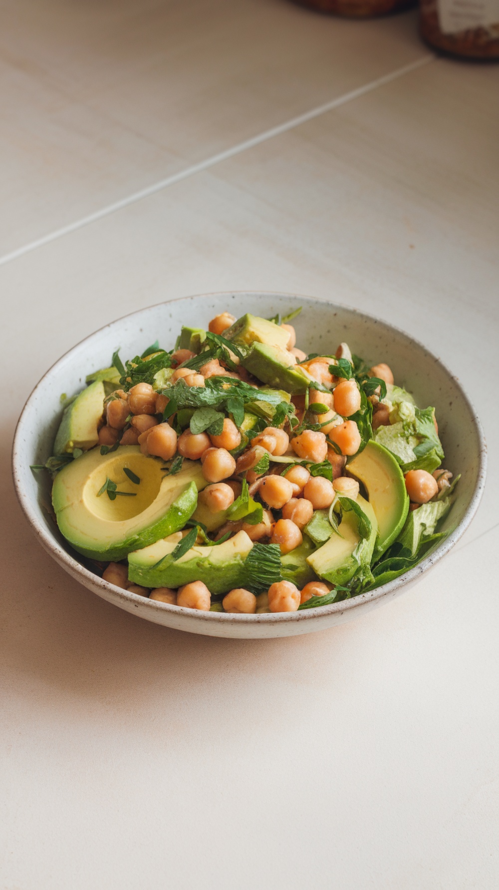 A bowl of chickpea and avocado salad with greens and herbs.