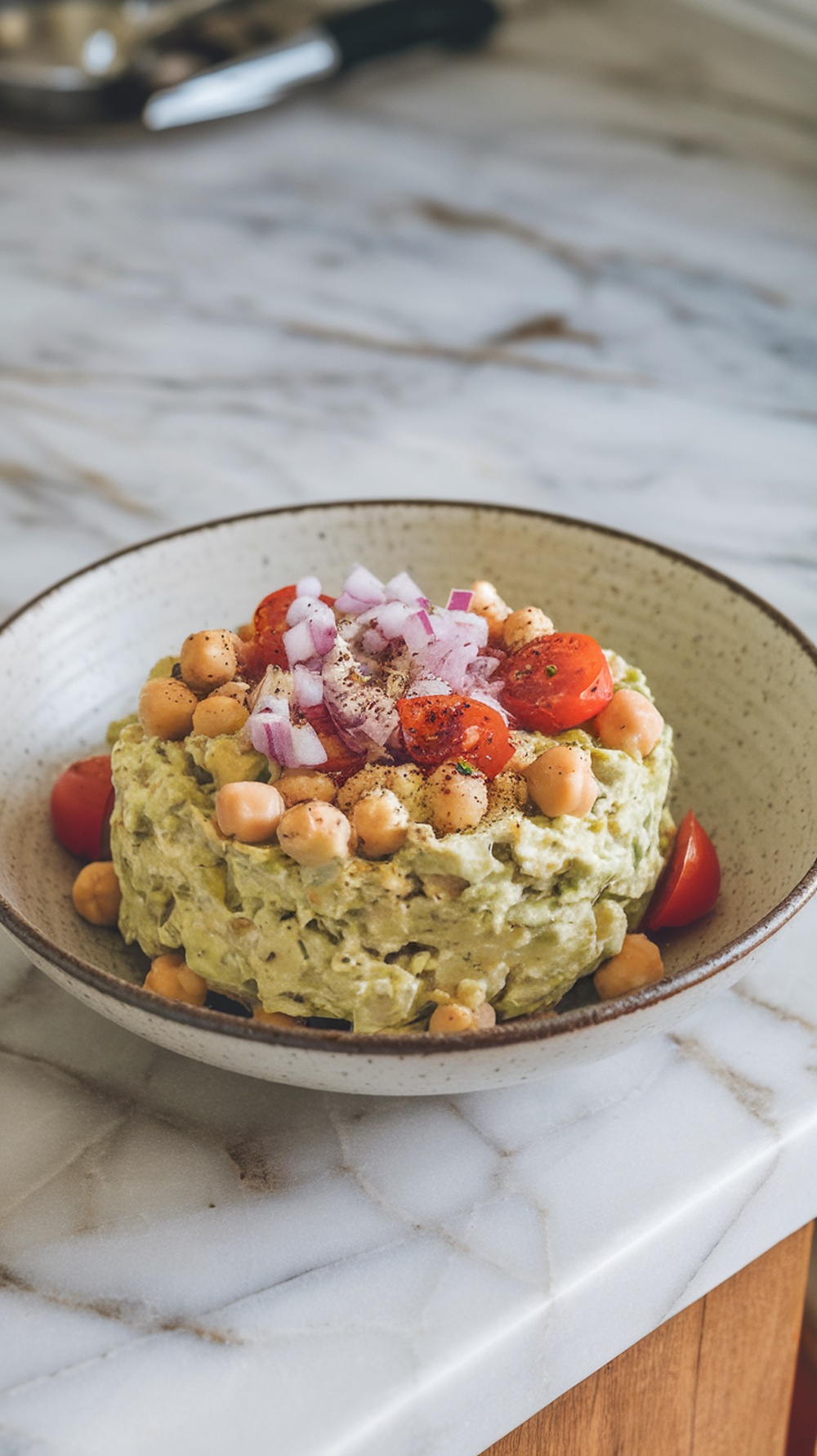 A bowl of creamy avocado and chickpea salad topped with cherry tomatoes and red onion.